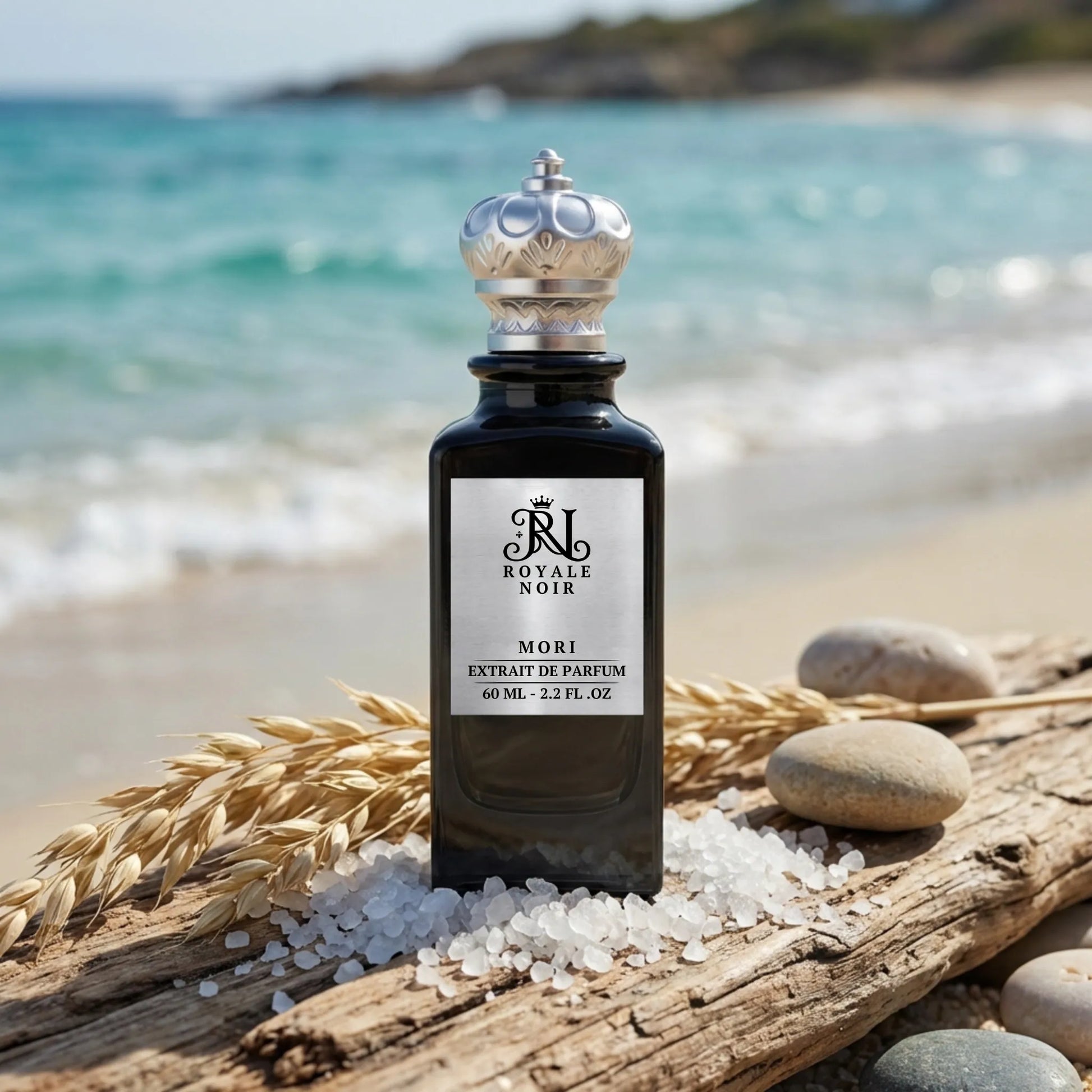 A black perfume bottle labeled "Royale Noir Mori Extrait de Parfum, 60 ml - 2.2 fl. oz" on a beach with ocean in the background